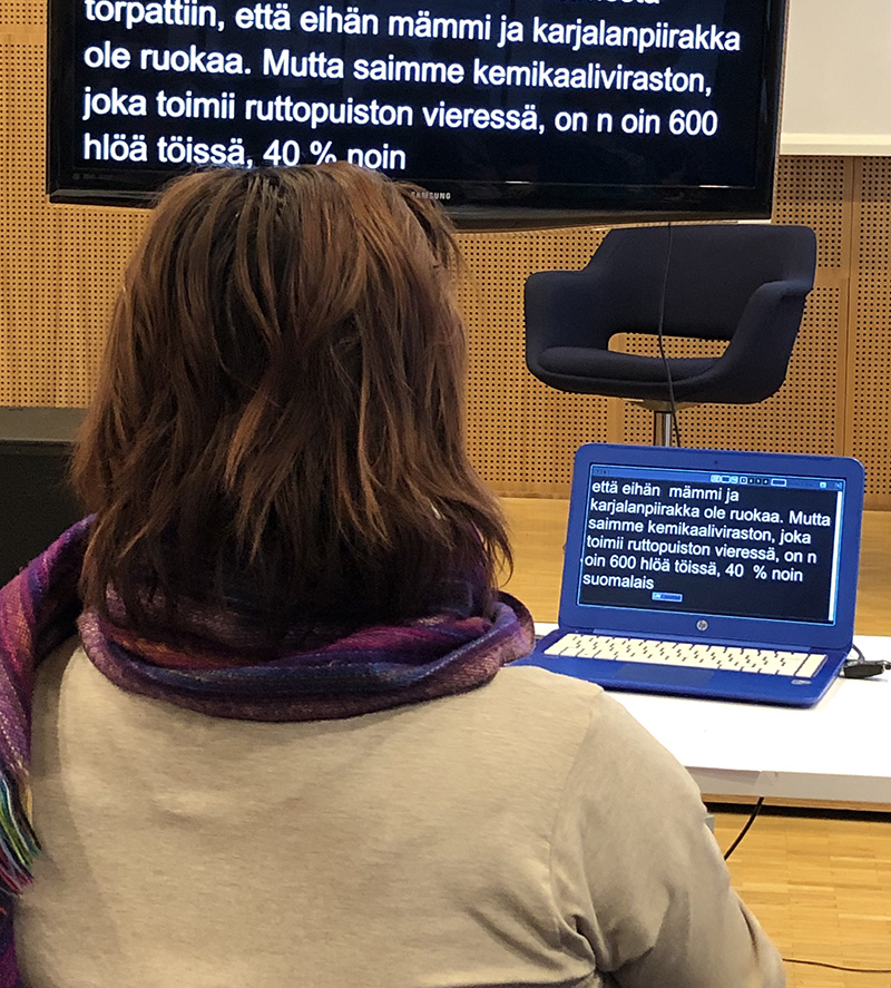 Kirjoitustulkki työssään. Edessä näkyy kannettava tietokone ja televisio.